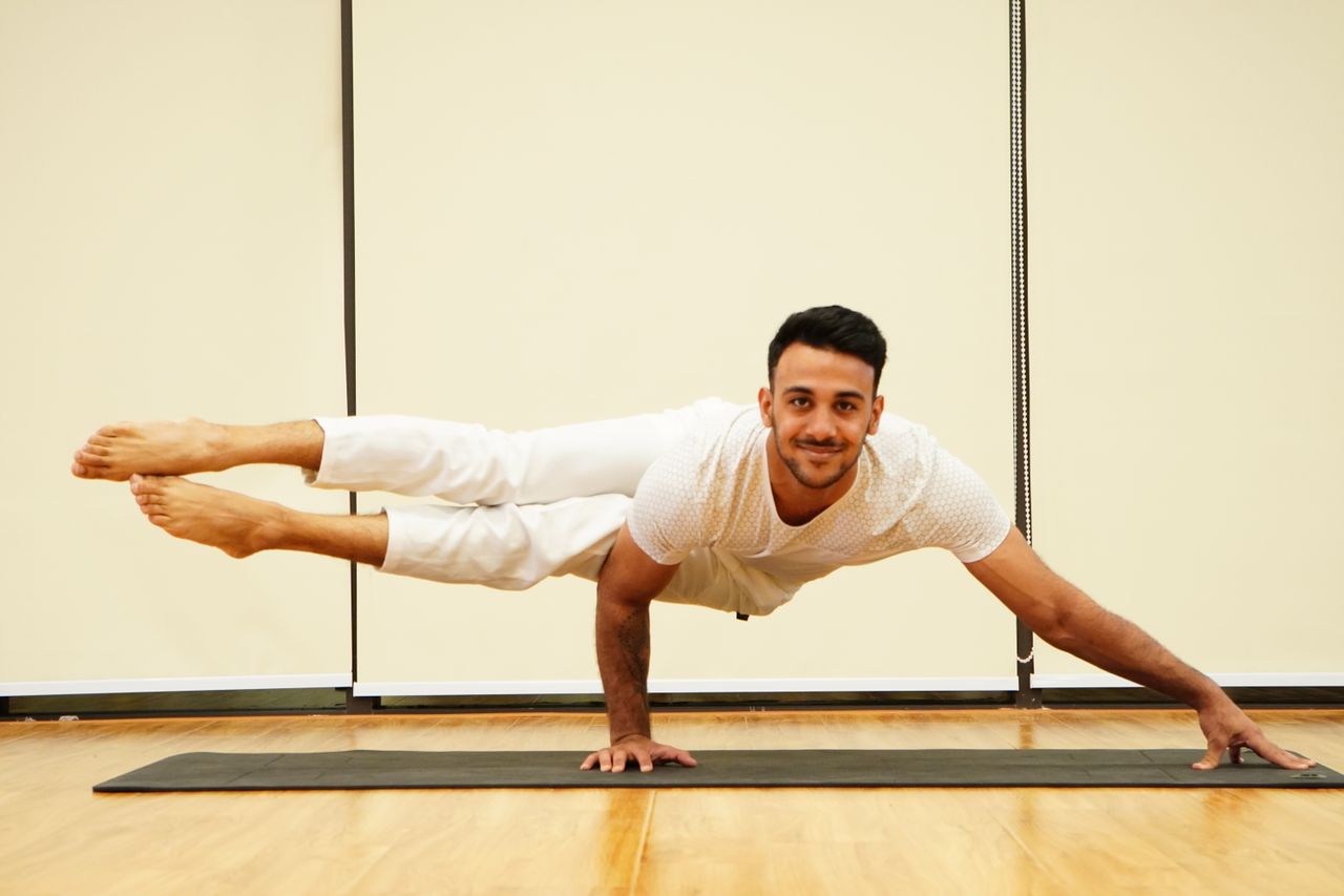 who-we-are A man balances in an advanced yoga pose on a mat indoors, showcasing strength and focus.
